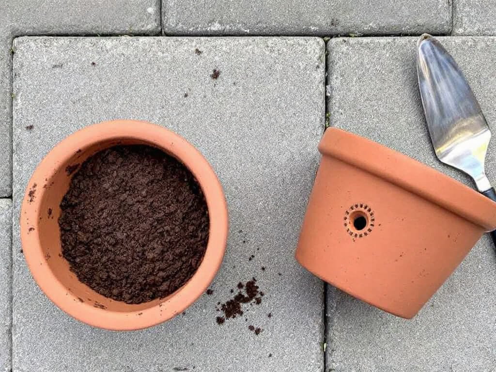 Terracotta pot filled with potting mix, ready for sowing cilantro, beside an upturned pot with a drainage hole