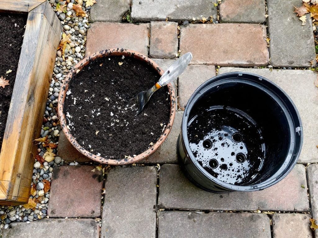 A pot filled with dark perlite and bark potting mix beside an upturned pot showing drainage holes, ready for strawberries.